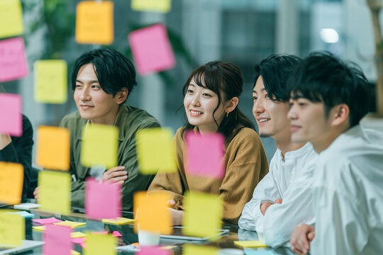 付箋を貼ったガラス越しに話し合う若いチーム